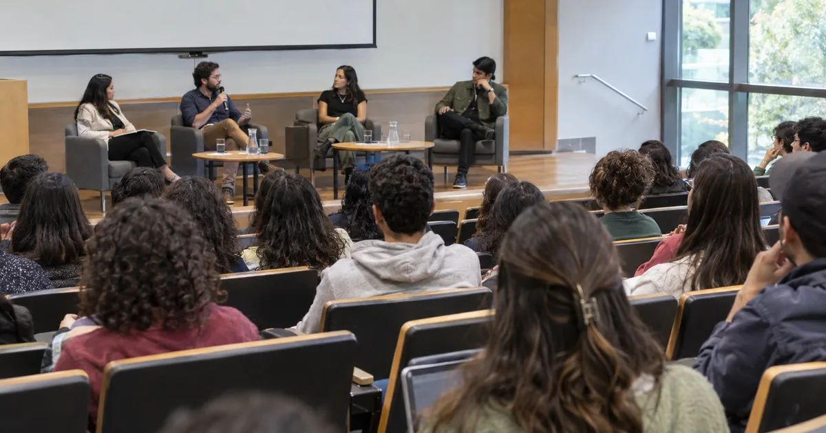 Imagen generada con IA: asistentes a un auditorio universitario durante un panel de discusión (escena ilustrativa con personas ficticias)